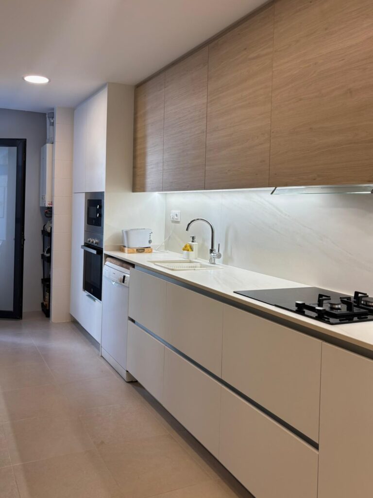 Cocina lineal blanca con encimera veteada y luces LED bajo armarios