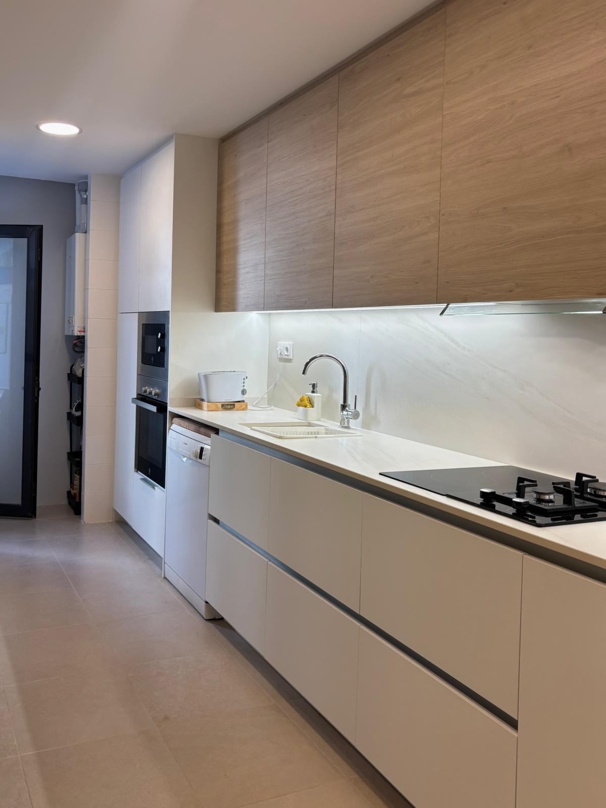 Cocina lineal blanca con encimera veteada y luces LED bajo armarios